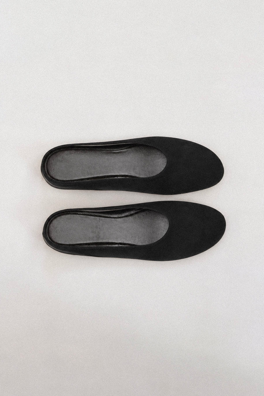 A pair of black flat shoes with a matte finish, shown from a top-down view on a light gray background.